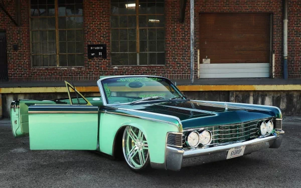 HD PC desktop wallpaper featuring a classic mint green Lincoln convertible parked in front of an industrial brick building with open driver-side door.