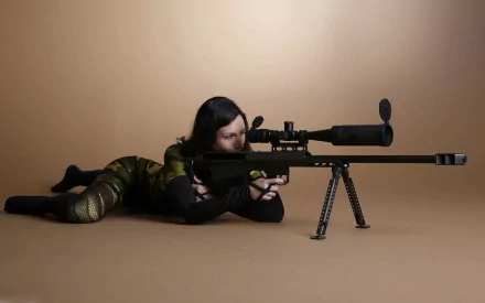 A sniper in camouflage lies prone, aiming through the scope of a large sniper rifle in a minimalist, brown-toned setting. This HD desktop wallpaper showcases a military-themed background.
