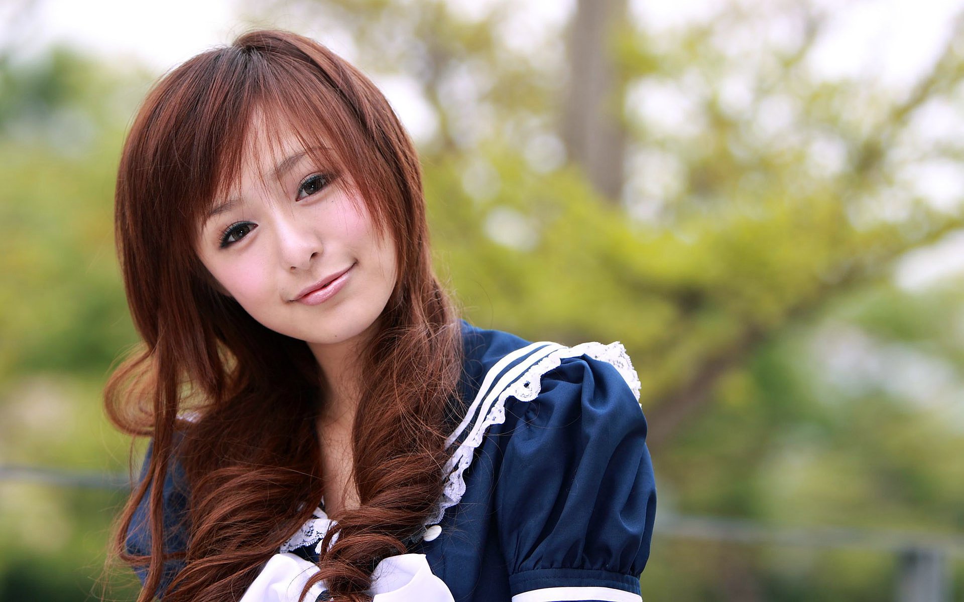 A woman with long brown hair smiles in a blue dress, surrounded by greenery. This HD image serves as a striking desktop wallpaper and background.