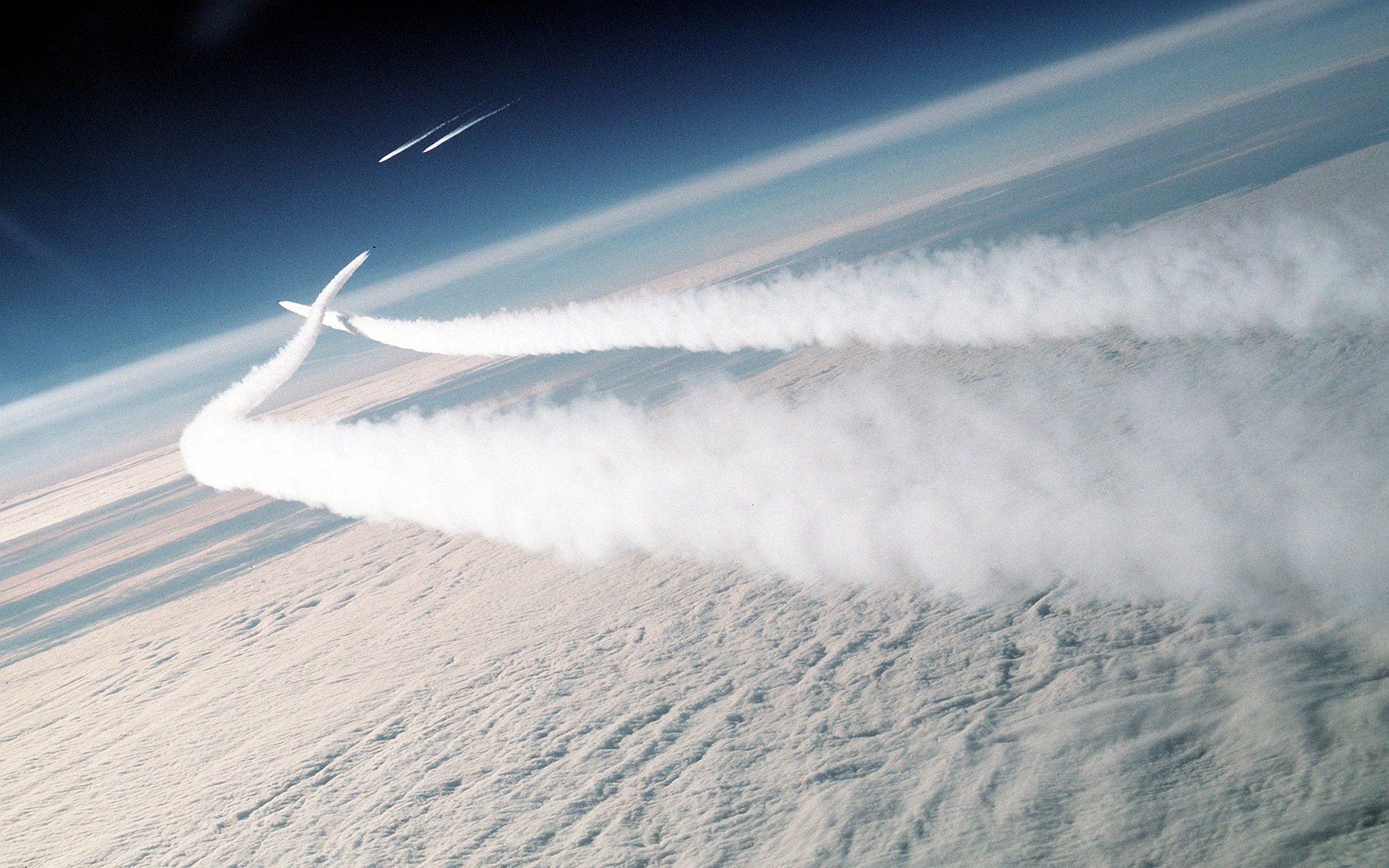 HD desktop wallpaper of an aircraft soaring through the sky, leaving thick white contrails against a backdrop of clouds.