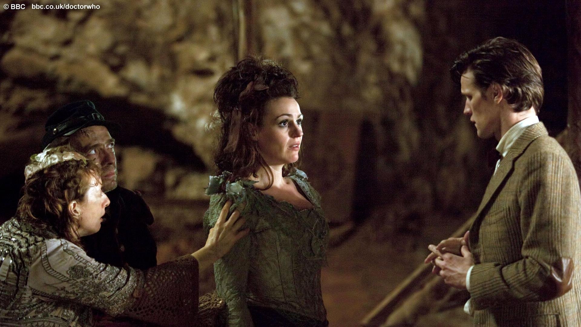 HD desktop wallpaper featuring a scene from the TV show Doctor Who (2005) with characters engaged in a tense moment inside a dimly lit cave.