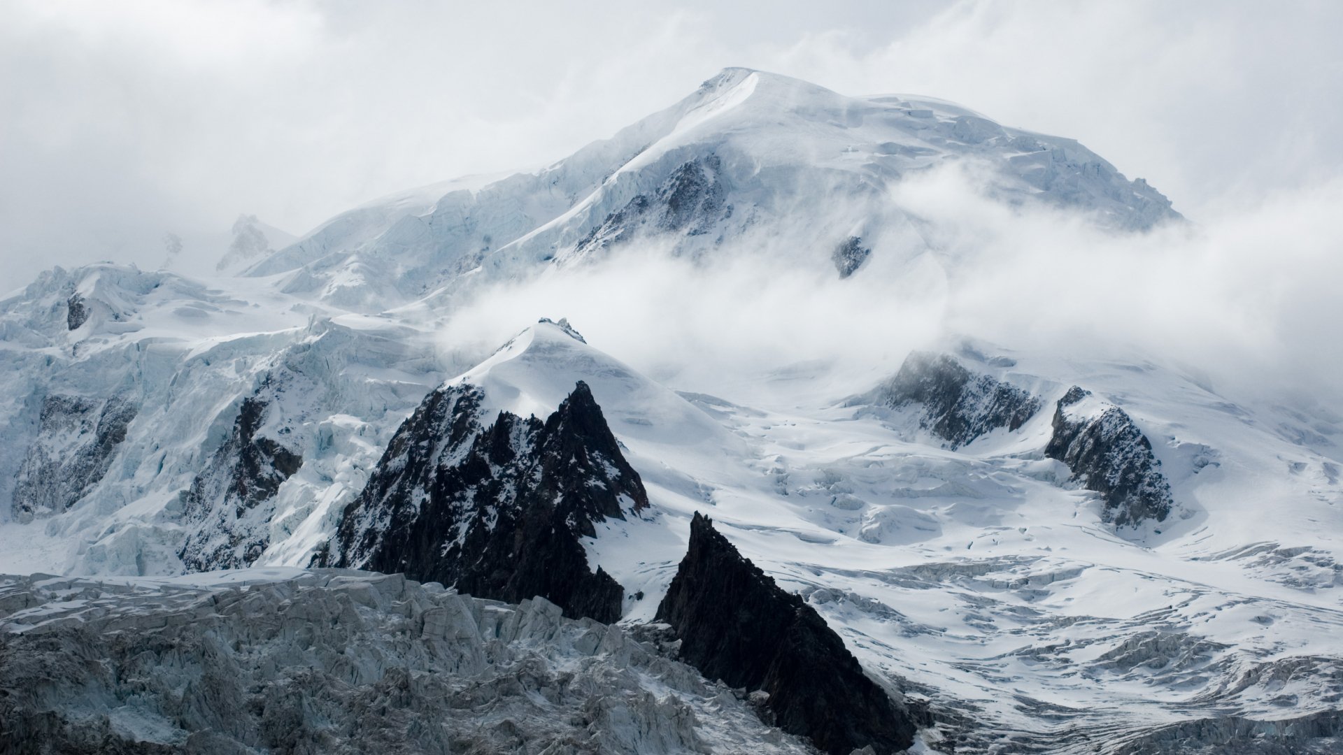 HD PC desktop wallpaper featuring a majestic snow-covered mountain landscape partially shrouded in mist and clouds, showcasing nature's rugged beauty.