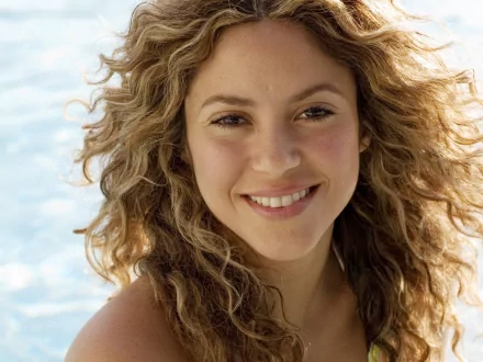 HD PC desktop wallpaper featuring a close-up of Shakira smiling with natural curly hair against a bright, soft-focused background, highlighting her musical appeal.