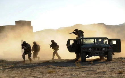 HD PC desktop wallpaper showing U.S. Army Infantry soldiers advancing in a dusty war zone, with one soldier taking position on a military Humvee.