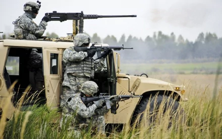 HD PC desktop wallpaper featuring soldiers in military gear positioned around a tactical vehicle in a grassy field, part of an active combat scene.