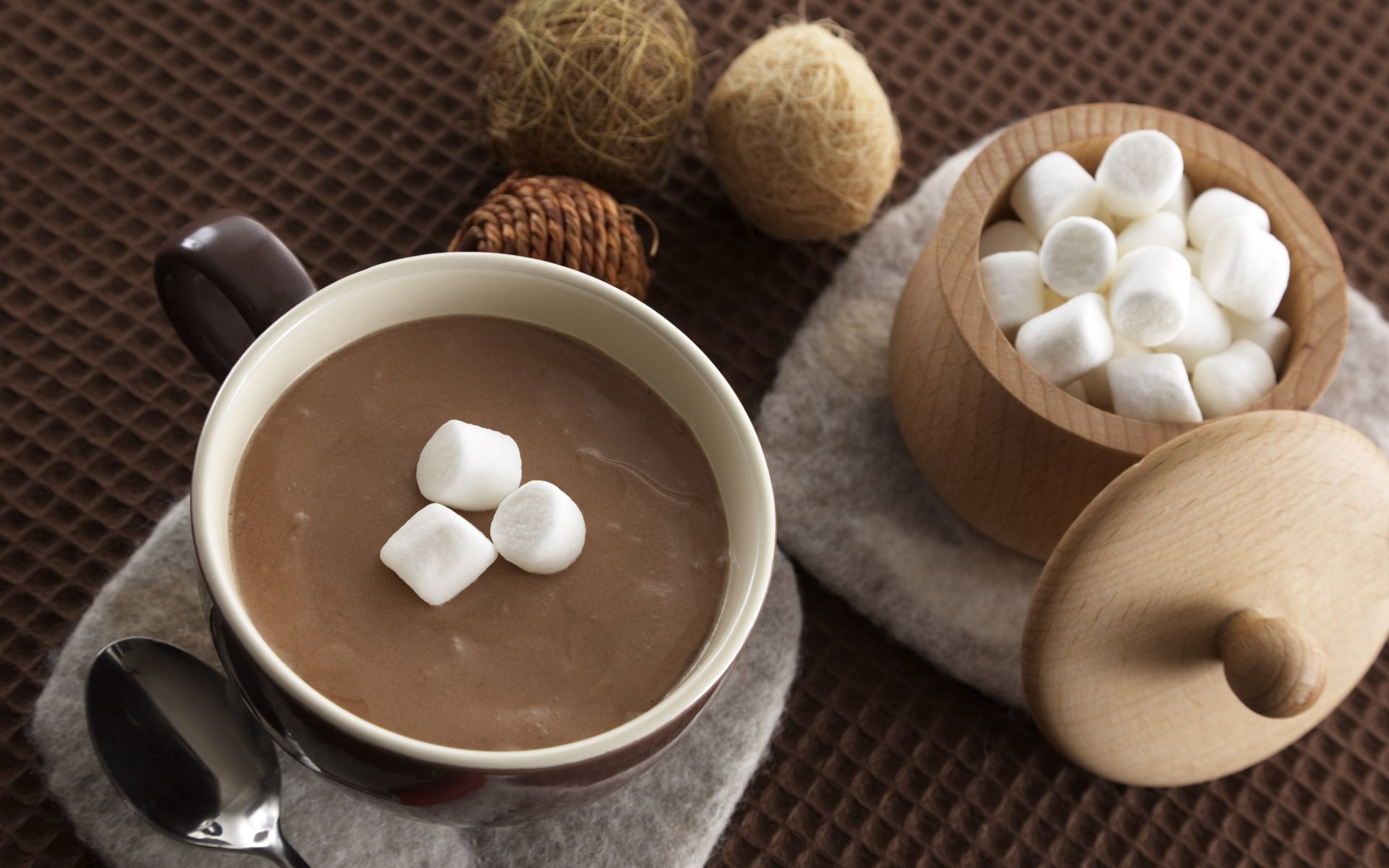 HD PC desktop wallpaper featuring a warm cup of coffee topped with marshmallows, accompanied by a wooden jar filled with extra marshmallows on a textured brown surface.