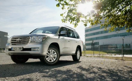 HD PC desktop wallpaper background featuring a silver Toyota SUV parked by a modern office building with sunlit trees overhead.