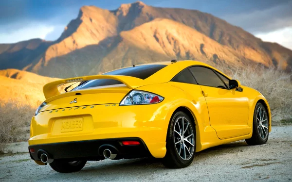 Yellow Mitsubishi Eclipse parked on a dirt road with mountains in the background, captured in HD for a vivid PC desktop wallpaper and background.
