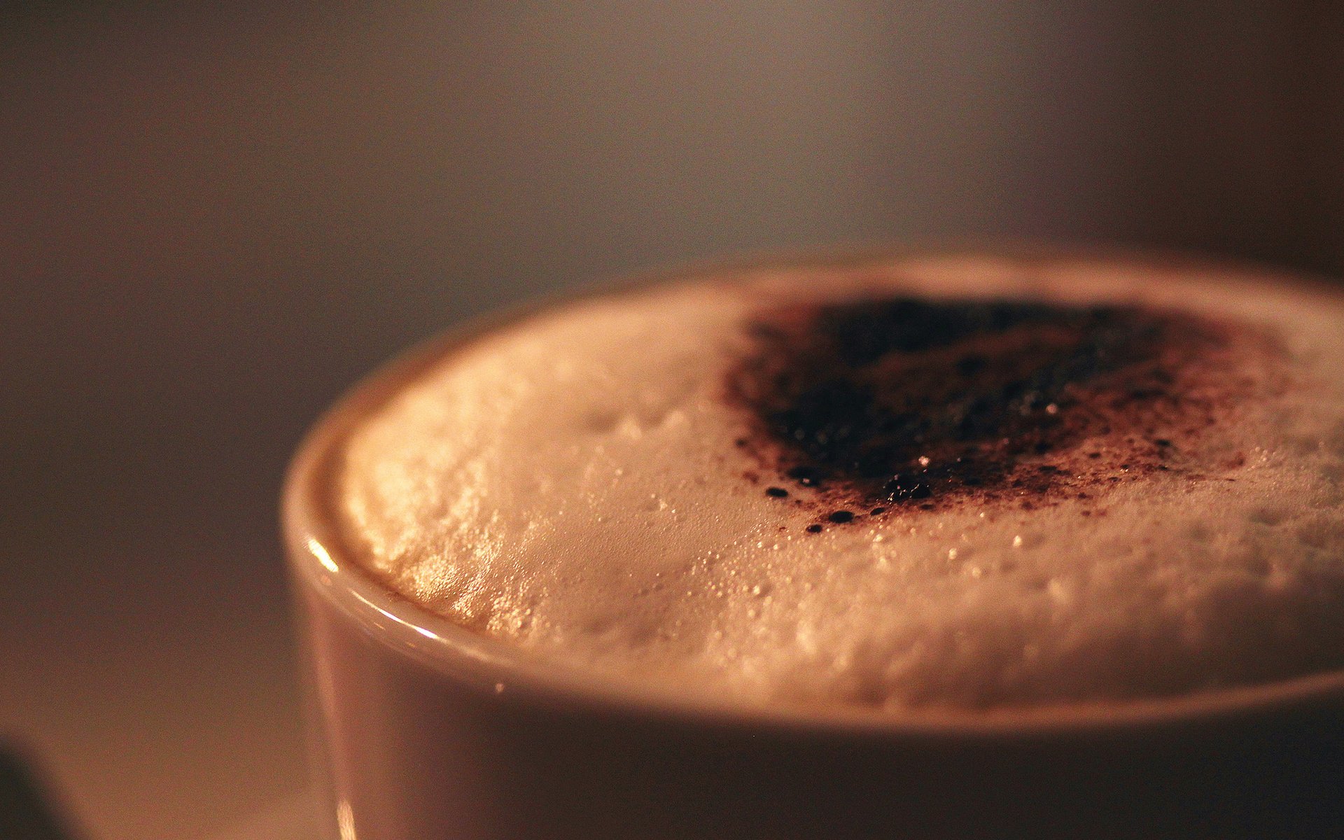 Close-up of a creamy cup of coffee topped with cocoa powder, set against a softly blurred background, creating an inviting atmosphere for this HD desktop wallpaper.