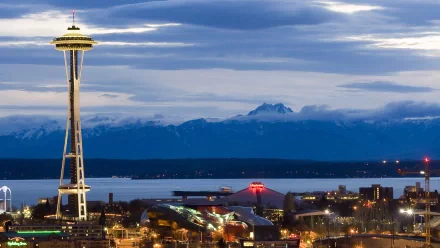 HD desktop wallpaper showcasing Seattle’s iconic man-made Space Needle against a backdrop of mountains and a cloudy sky at dusk.