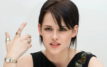 HD desktop wallpaper featuring celebrity Kristen Stewart with short dark hair, wearing a black sleeveless top, and gesturing with her hand.