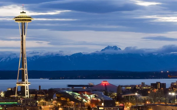 HD desktop wallpaper showcasing Seattle’s iconic man-made Space Needle against a backdrop of mountains and a cloudy sky at dusk.