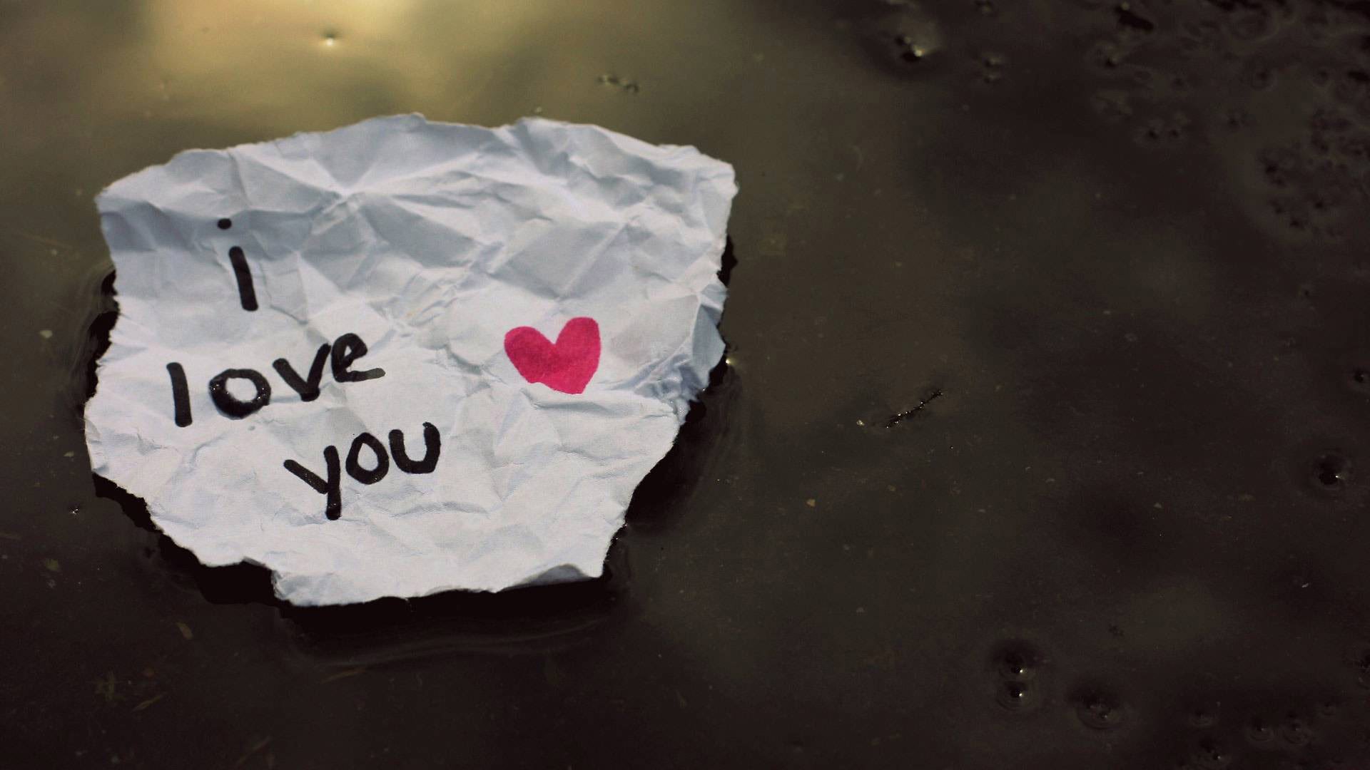 Artistic HD desktop wallpaper featuring a crumpled paper with I love you and a pink heart on a dark textured background, expressing love.
