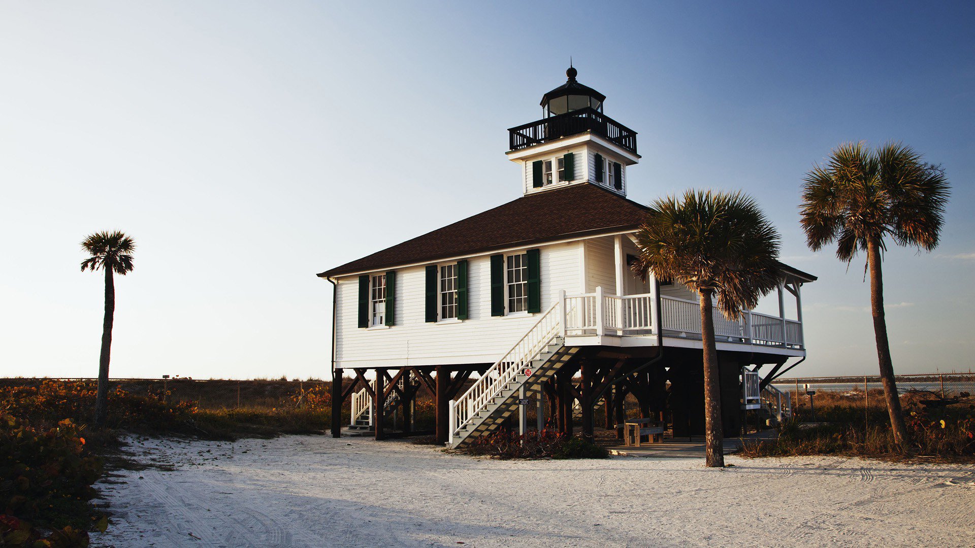 HD desktop wallpaper featuring a man-made elevated house with palm trees against a clear blue sky, blending coastal architecture with natural scenery.