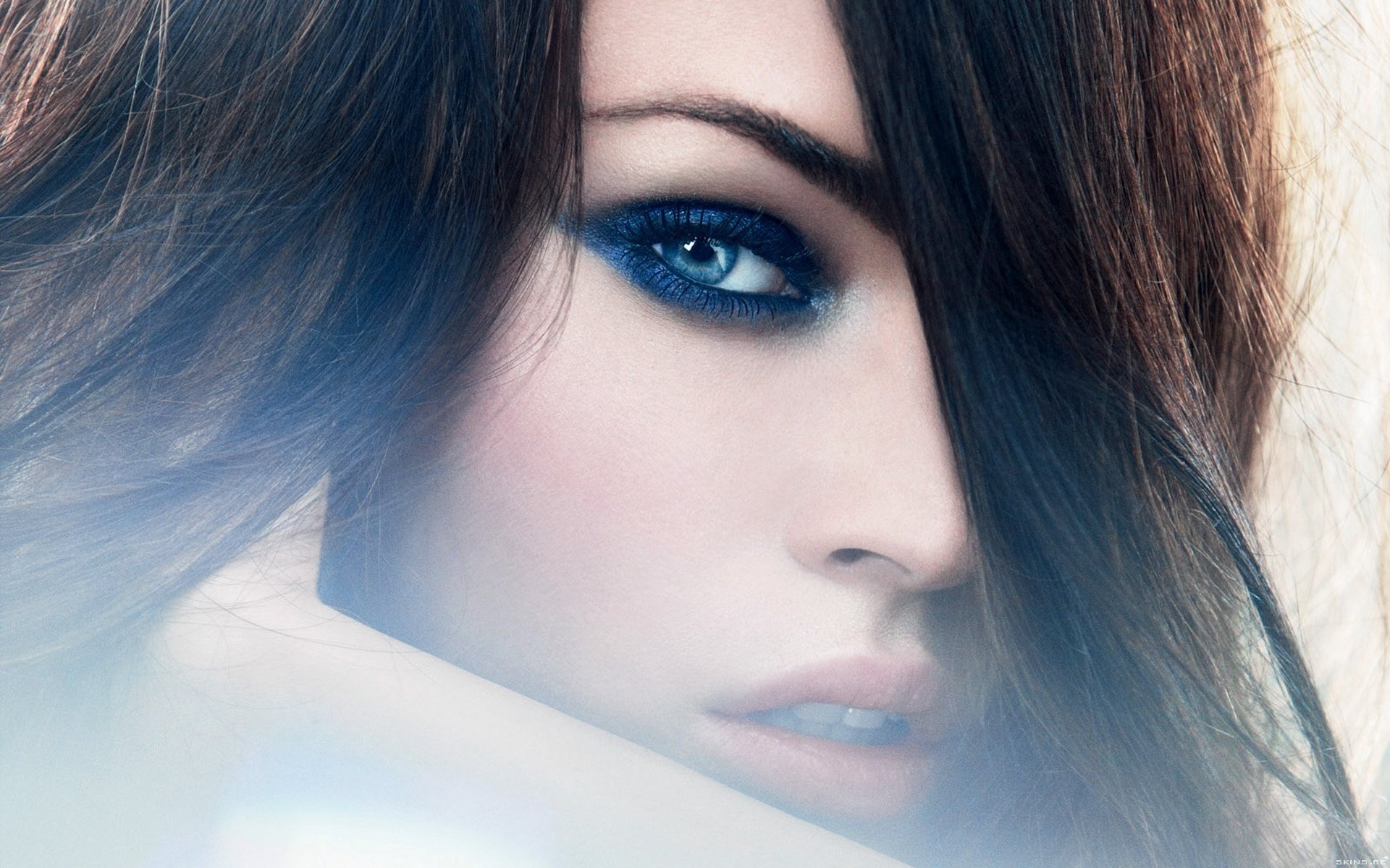 An artistic HD wallpaper of a woman with striking blue eye makeup and soft lighting, creating a captivating and serene background.