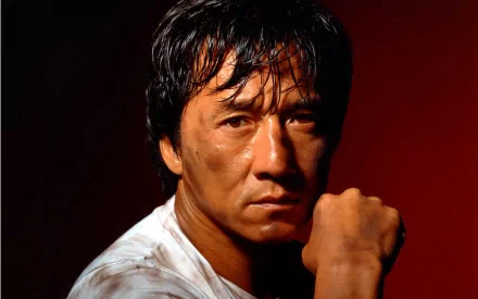 HD desktop wallpaper of celebrity Jackie Chan, showcasing a close-up portrait with a serious expression and a dark red background.