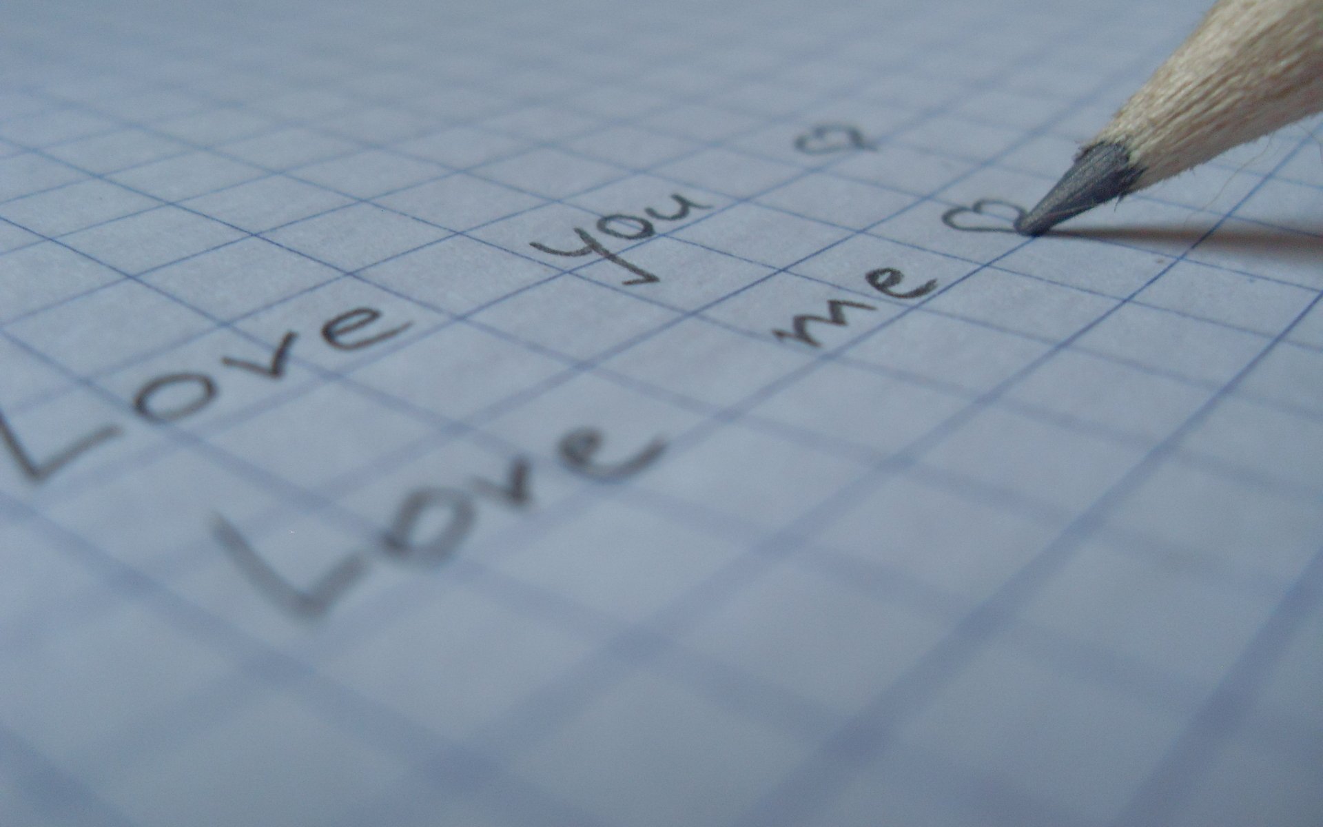A close-up of handwritten notes on grid paper, featuring the phrases Love you and Love me, accented with a heart, creating an artistic expression of love. HD desktop wallpaper.