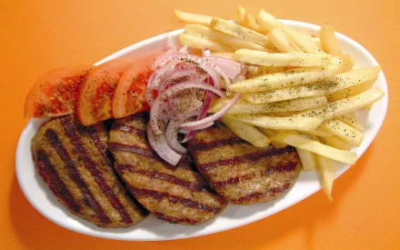 HD desktop wallpaper featuring a meal of grilled pork patties, sliced tomatoes, onions, and seasoned French fries on a white plate against an orange background.