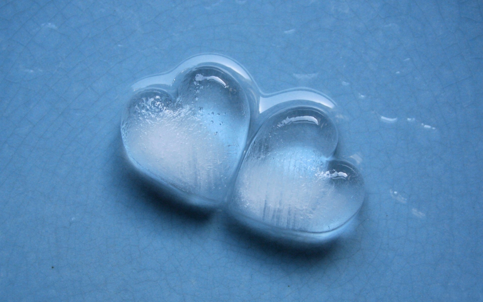 Two clear ice hearts sit on a soft blue surface, creating a visually striking and artistic representation of love. This image makes for a captivating HD desktop wallpaper.