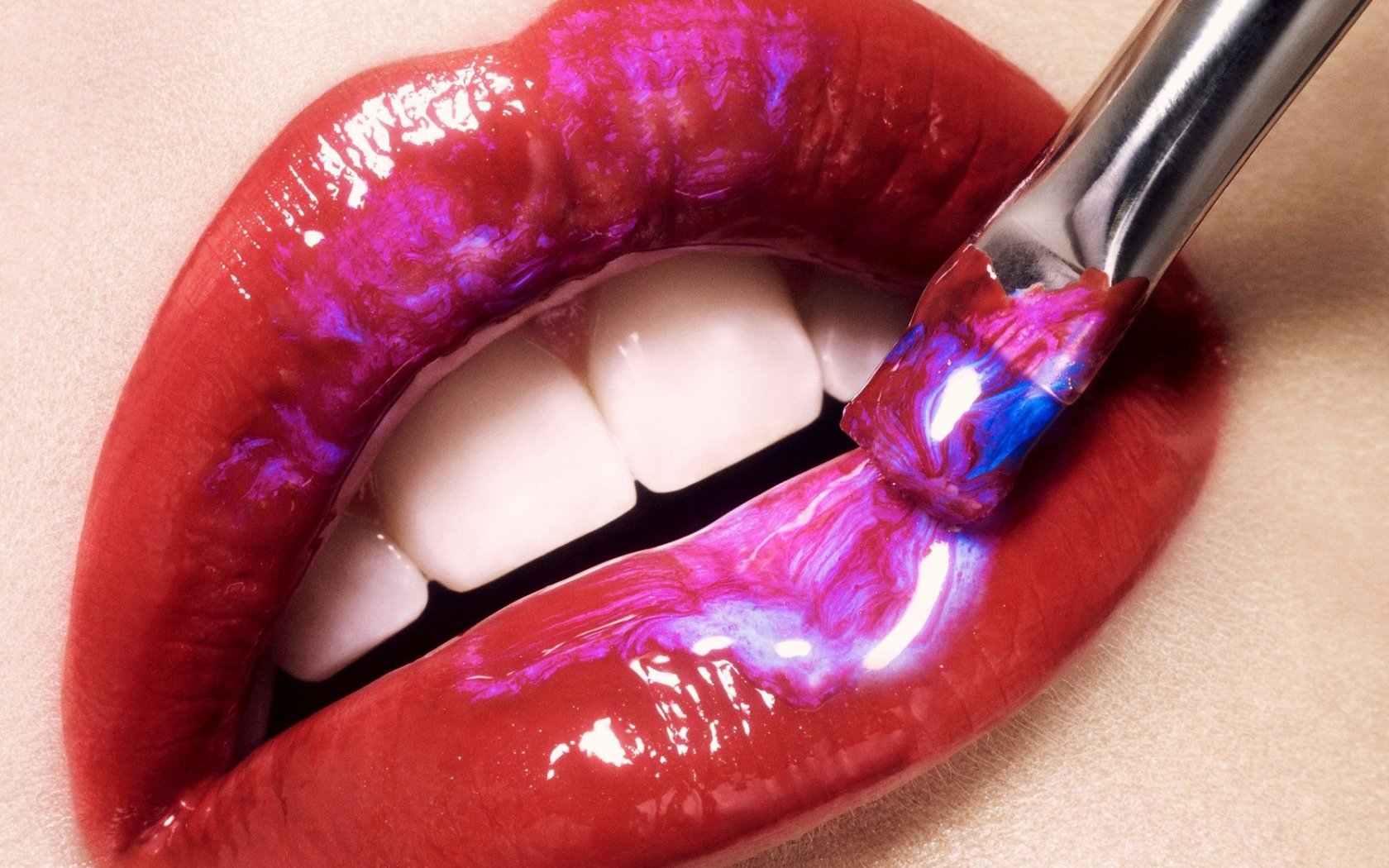 Close-up of a woman's lips, featuring glossy red color and vibrant, iridescent highlights, as a brush applies shimmering product. A striking HD desktop wallpaper and background.