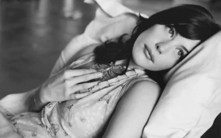 A stunning black and white HD wallpaper featuring actress Liv Tyler, captured in a contemplative moment, lying on a bed with a soft expression on her face.