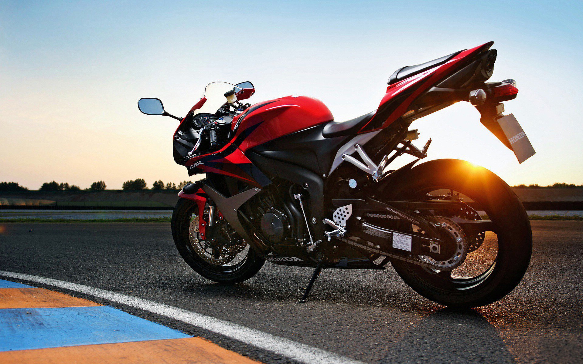 HD desktop wallpaper featuring a sleek red Honda sport motorcycle parked on a racetrack at sunset.