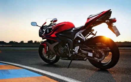 HD desktop wallpaper featuring a sleek red Honda sport motorcycle parked on a racetrack at sunset.
