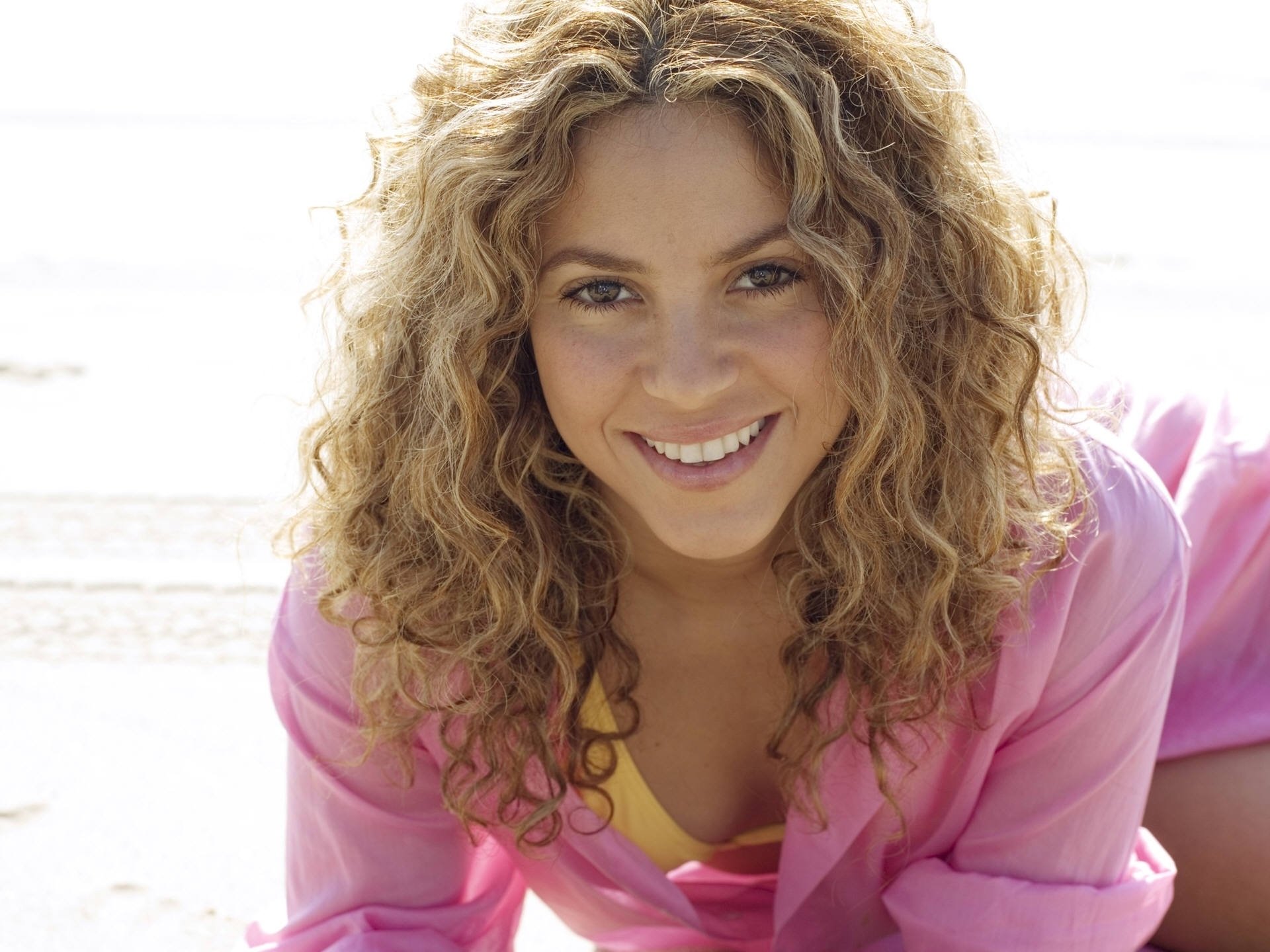 A joyful Shakira smiles warmly, showcasing her signature curly hair, in this vibrant HD desktop wallpaper background, celebrating her connection to music.