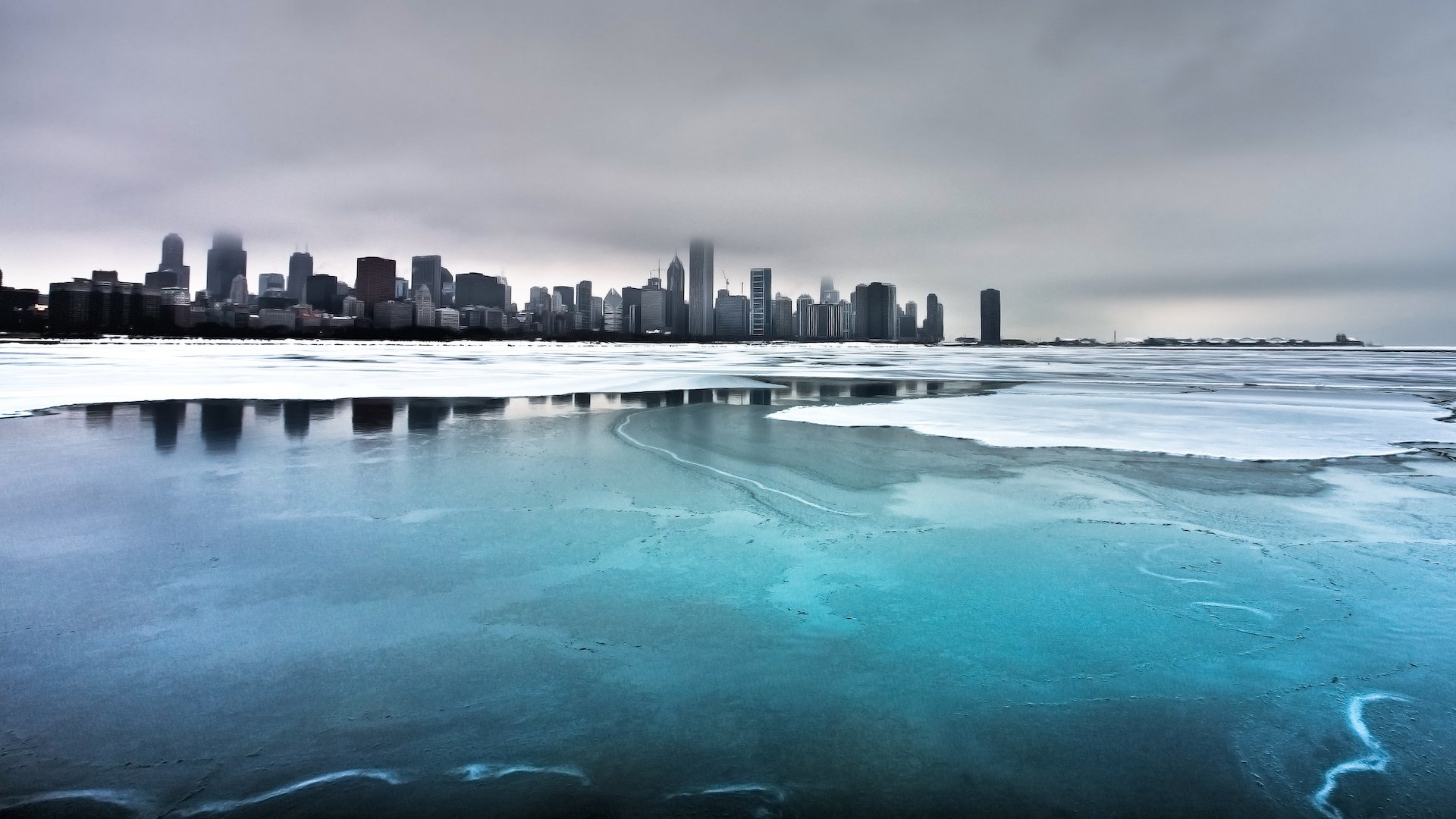 Frozen icy river under a cold blue winter sky with Chicago's city skyline and snow-covered land in the background, capturing a serene man-made landscape.