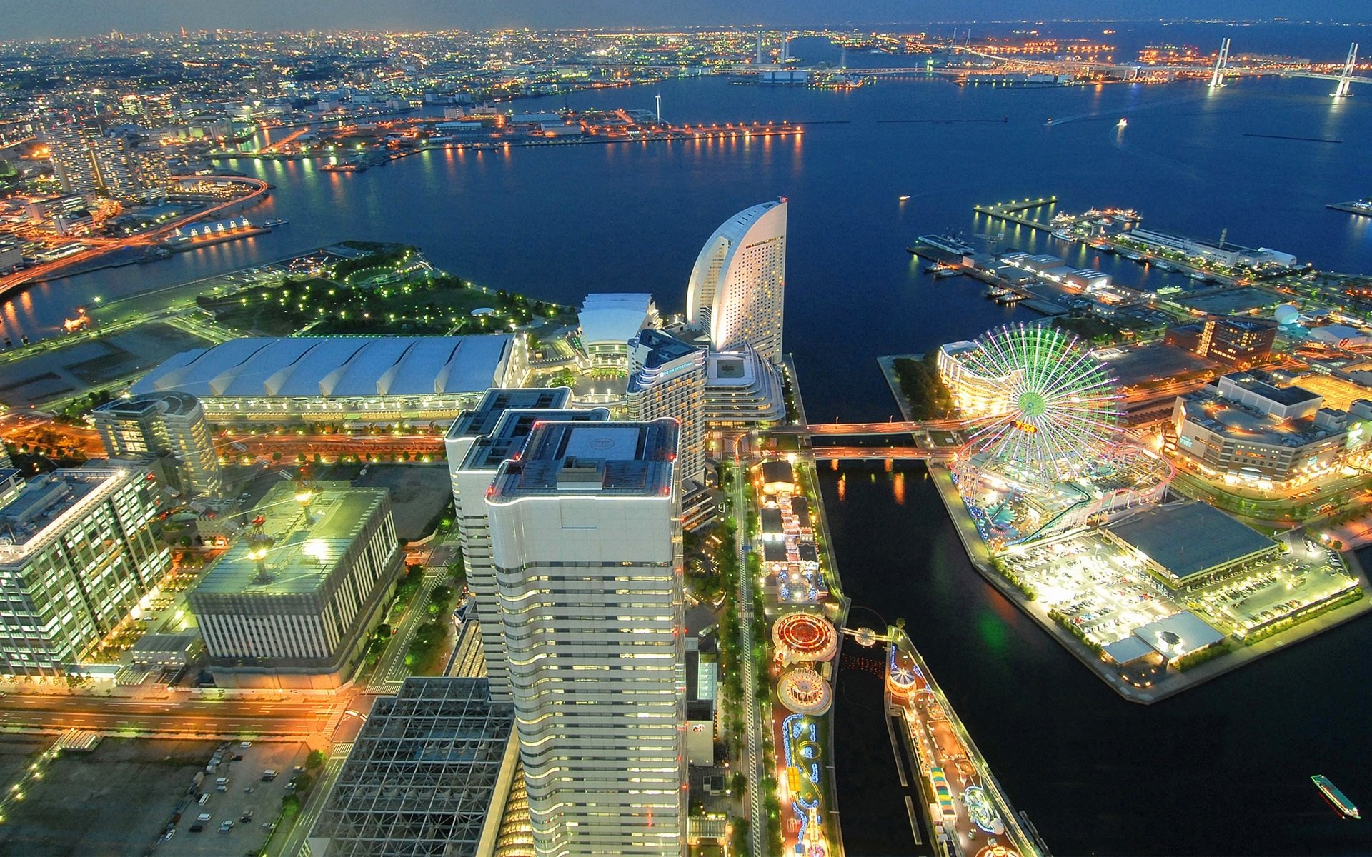 A stunning HD desktop wallpaper featuring a vibrant view of Yokohama, Japan at night, showcasing illuminated skyscrapers, a ferris wheel, and a bustling waterfront.