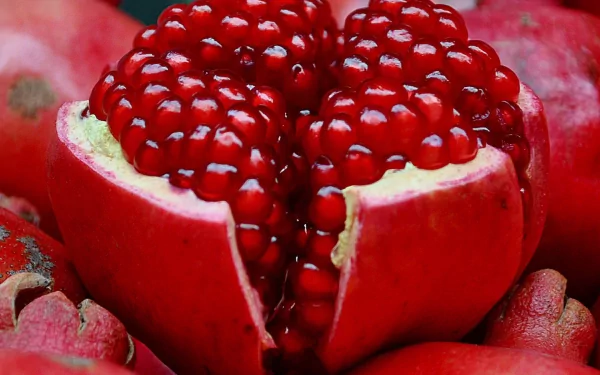HD desktop wallpaper featuring a close-up of a vibrant, juicy pomegranate with bright red seeds and surrounding whole pomegranates in the background.