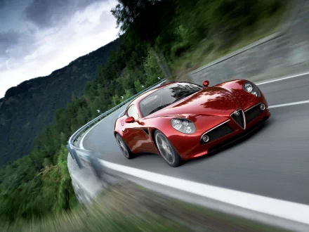 HD PC desktop wallpaper featuring a red Alfa Romeo 8C Competizione driving swiftly on a mountain road with lush greenery and cloudy sky in the background.
