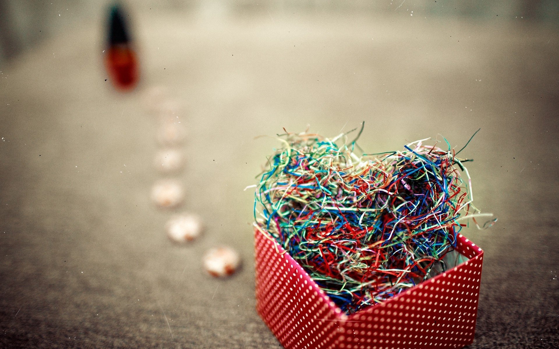 A vibrant, artistic heart made of colorful straw sits in a red box, set against a softly blurred background, evoking feelings of love and warmth in this HD desktop wallpaper.