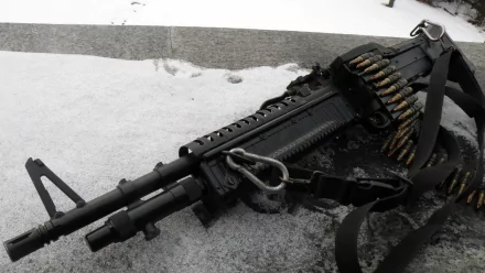 2K Quad HD PC desktop wallpaper: close-up of a man-made assault rifle with belt-fed ammunition resting on a snowy surface, high-contrast monochrome composition.