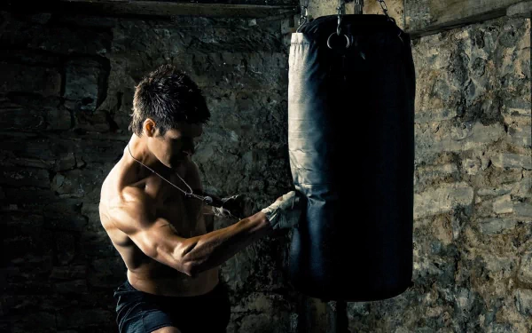 A high-definition wallpaper of a boxer intensely training with a punching bag in a dimly lit, rustic gym setting.