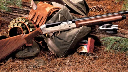 A shotgun rests on a bed of pine needles, surrounded by ammunition, gloves, and hunting gear, creating a detailed HD desktop wallpaper and background.