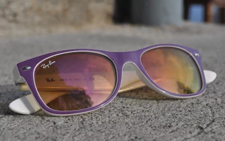 Close-up of purple Ray-Ban sunglasses on pavement with skyline reflection — 2K Quad HD PC desktop wallpaper, man-made object.