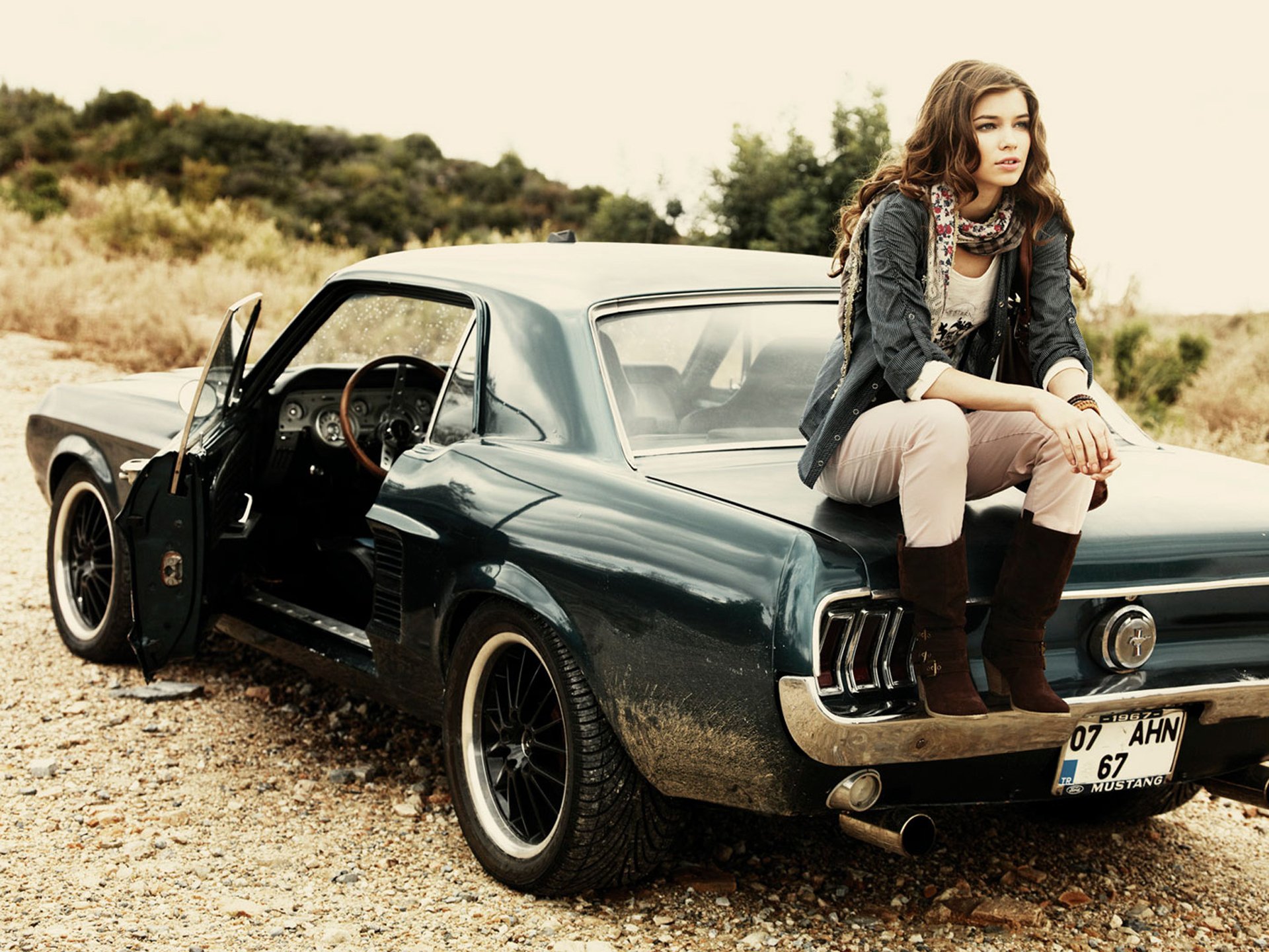 A woman casually sits on a classic Mustang in a scenic outdoor setting, embodying a relaxed, adventurous spirit. This HD photography serves as an eye-catching desktop wallpaper.