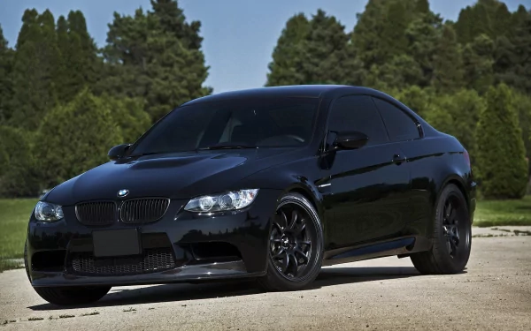 4K Ultra HD PC desktop wallpaper featuring a sleek black BMW vehicle parked on a sunlit road with green trees in the background.