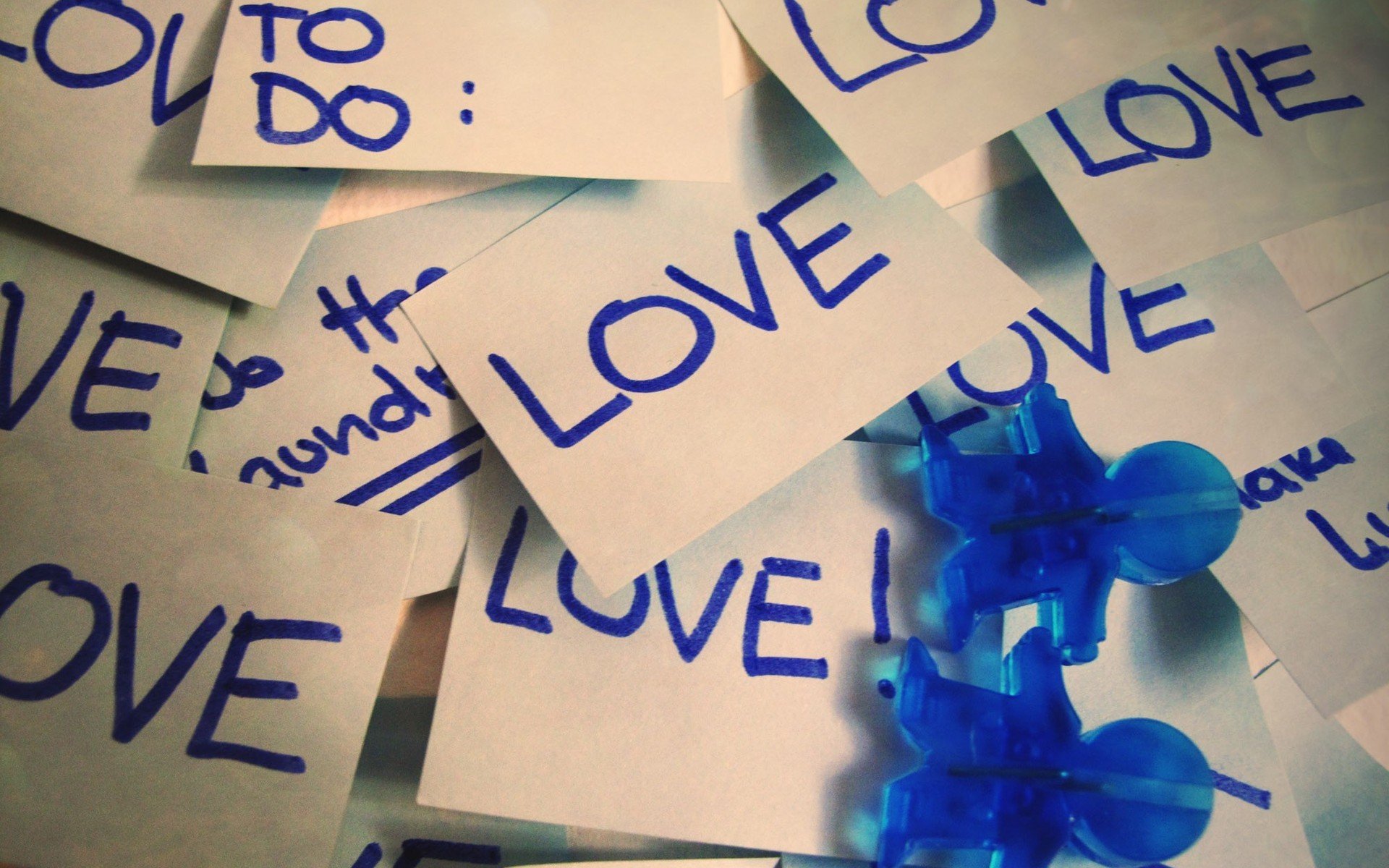 An artistic HD desktop wallpaper featuring scattered notes and blue pins, prominently displaying the word LOVE in vibrant blue ink, capturing a creative and affectionate vibe.