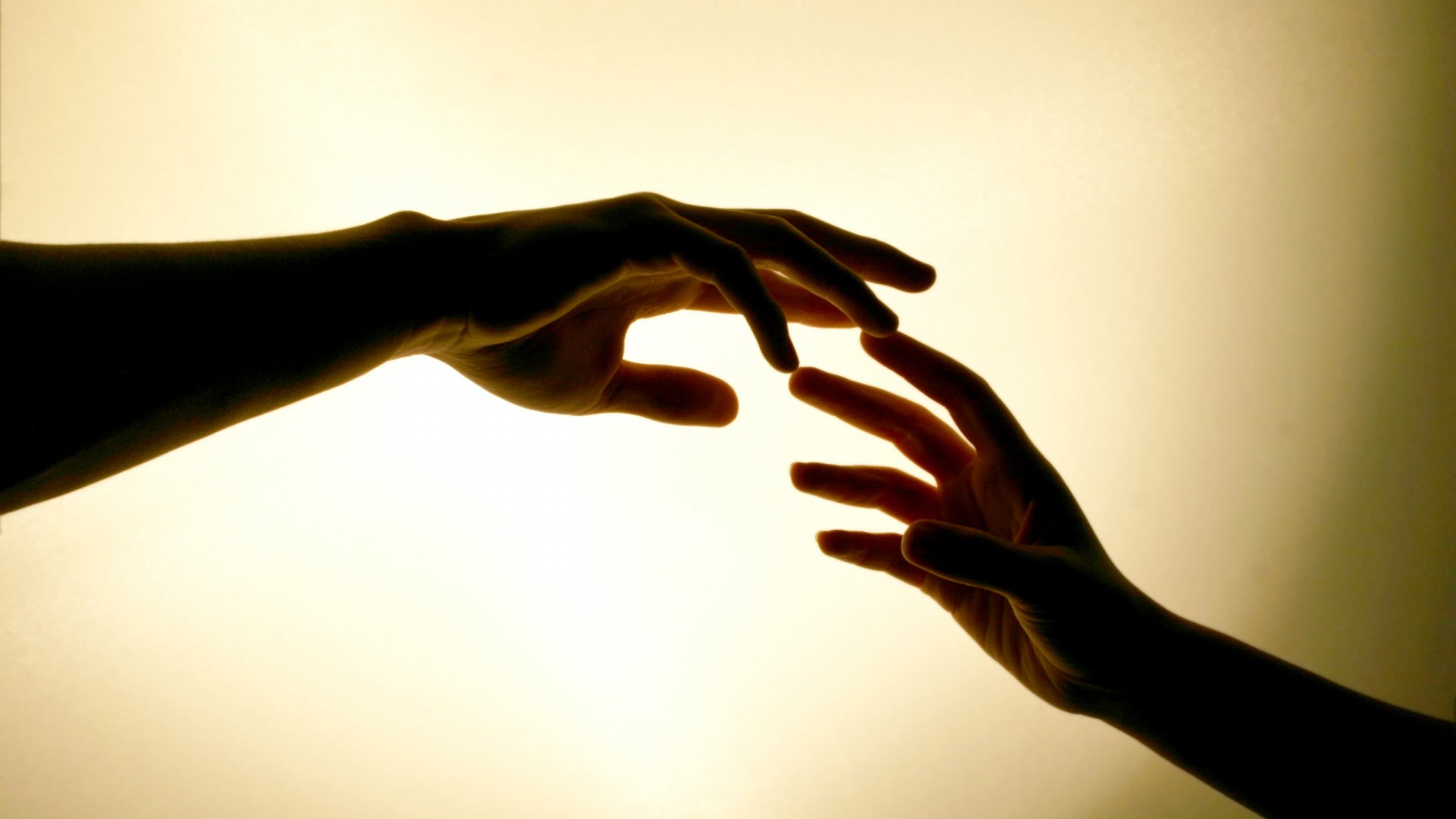 Silhouetted hands reaching toward each other against a warm, soft background, capturing a moment of connection and love in this HD PC desktop wallpaper.