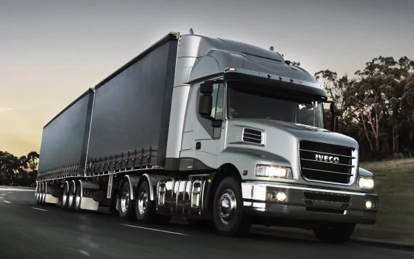 HD desktop wallpaper showcasing a sleek silver Iveco truck driving on a road with trees in the background, highlighting the powerful design of the vehicle.