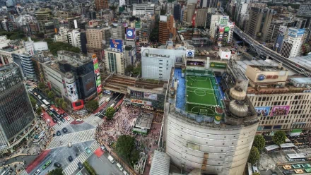HD PC desktop wallpaper/background: man-made Tokyo cityscape from above — bustling intersection, dense high-rises and a rooftop soccer field, vibrant urban details.