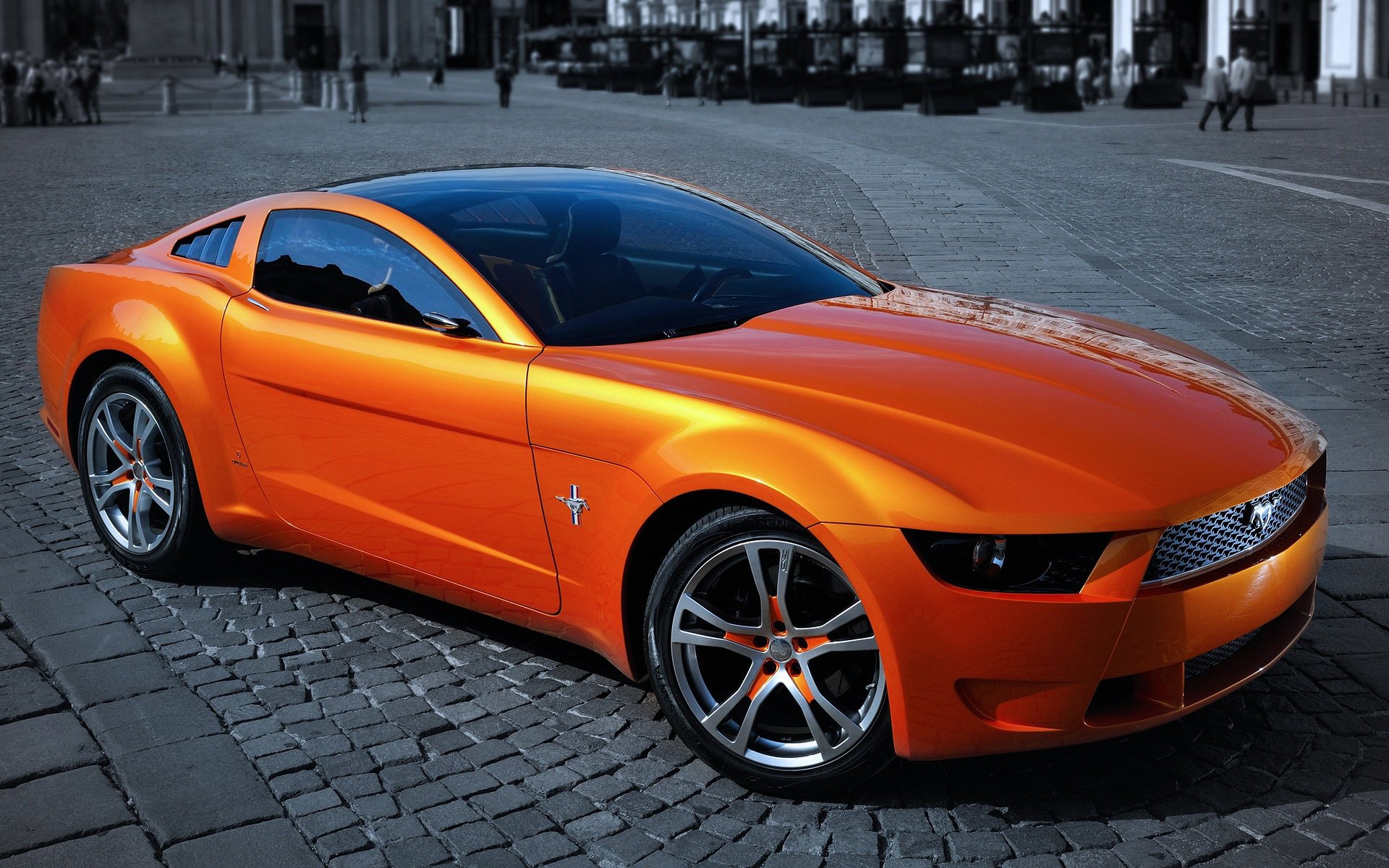 HD PC desktop wallpaper of an orange Ford sports vehicle on a cobblestone plaza, three-quarter front view.