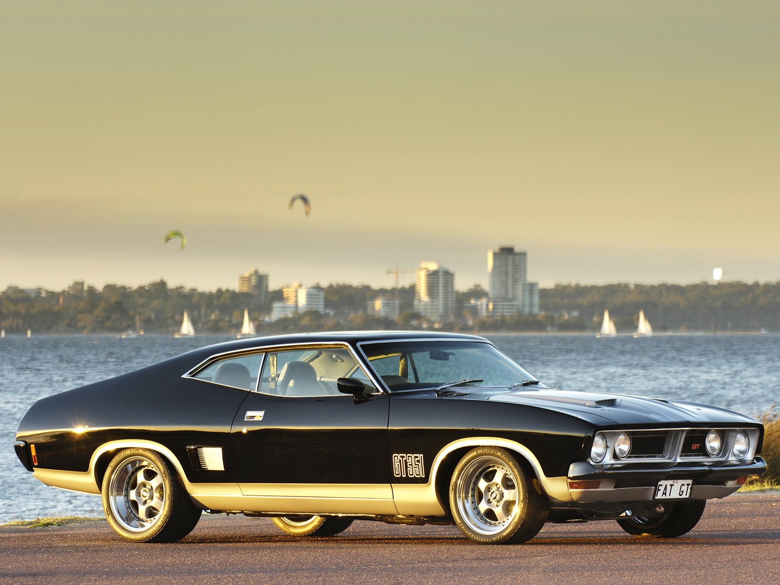 HD desktop wallpaper featuring a classic black Ford Falcon parked with a city skyline and water in the background.