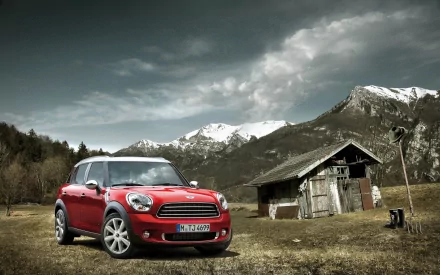 A vibrant red Mini Cooper parked in a scenic landscape, with snow-capped mountains in the background and a rustic cabin nearby, making for a striking HD PC desktop wallpaper.