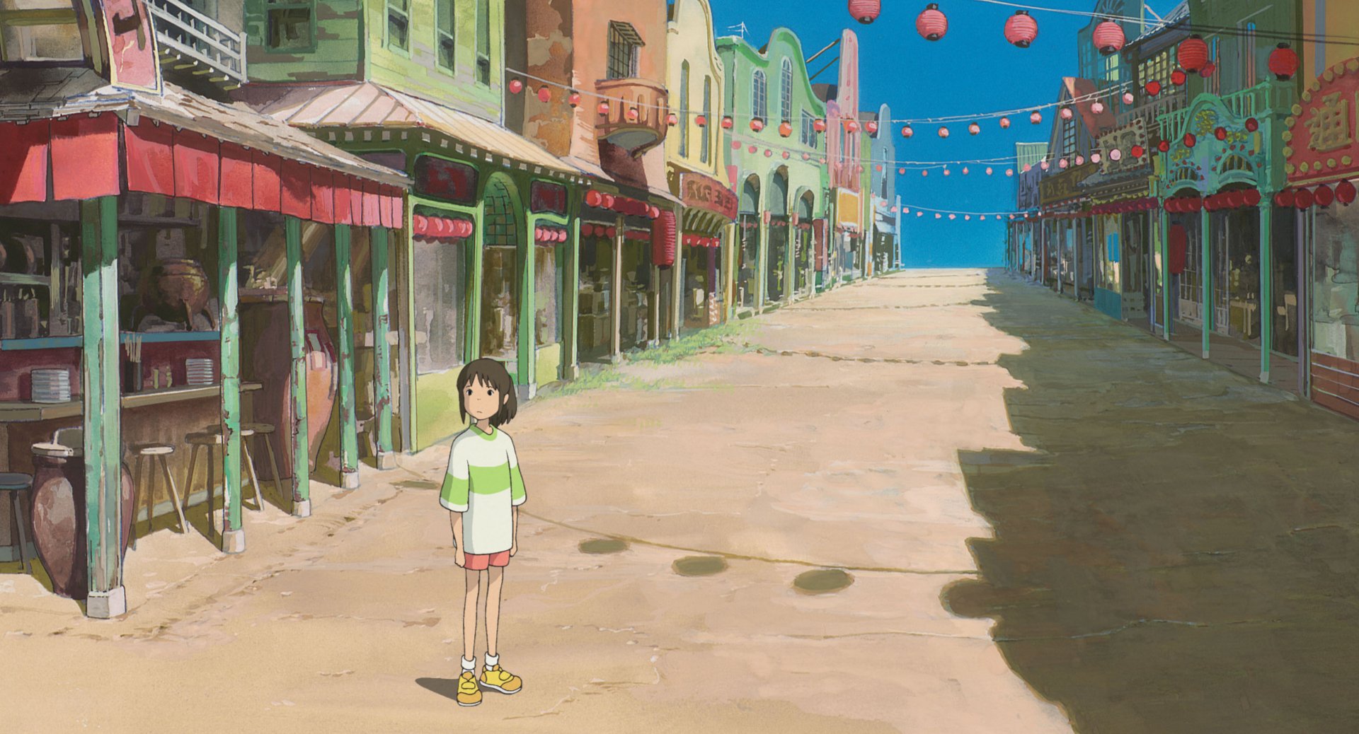A vibrant scene from Studio Ghibli's Spirited Away, featuring a young girl standing in a colorful, deserted street adorned with lanterns, showcasing the enchanting world of anime.