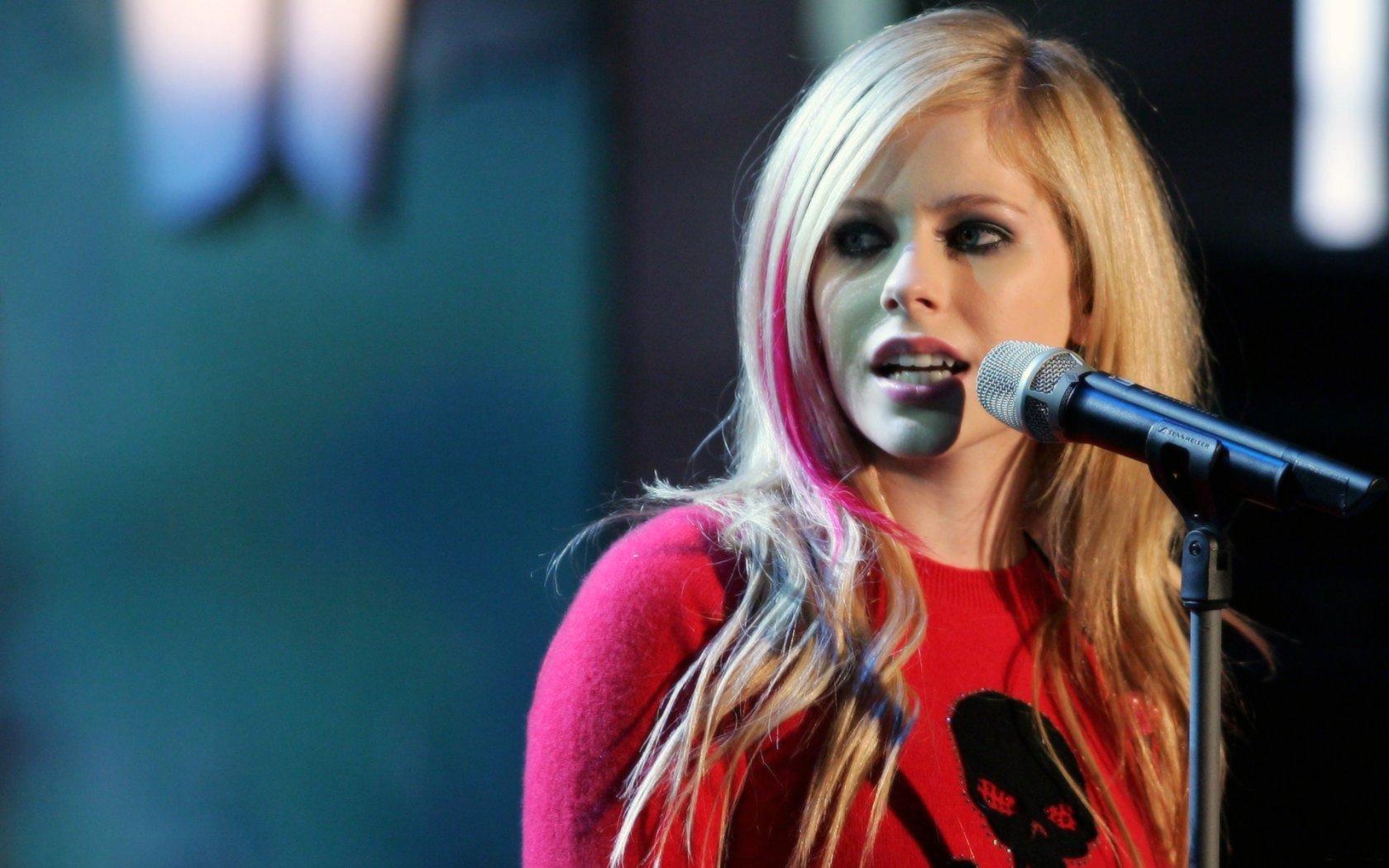 A high-definition desktop wallpaper featuring Avril Lavigne performing, with a microphone in hand and her iconic style highlighted, capturing her dynamic presence in music.