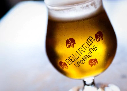 HD desktop wallpaper showing a close-up of a Delirium Tremens beer glass filled with golden beer, featuring the brand's pink elephant logo.