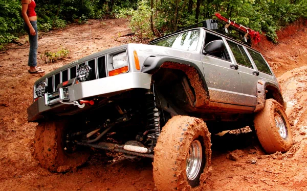 A rugged Jeep navigating a muddy trail, showcasing its off-road capabilities, surrounded by lush greenery—an exciting HD desktop wallpaper.